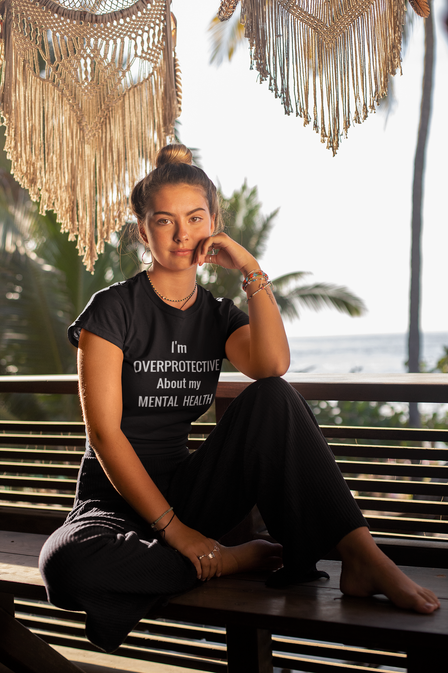 tee-mockup-of-a-woman-with-a-hair-bun-sitting-on-a-bench-by-the-beach-26863.png